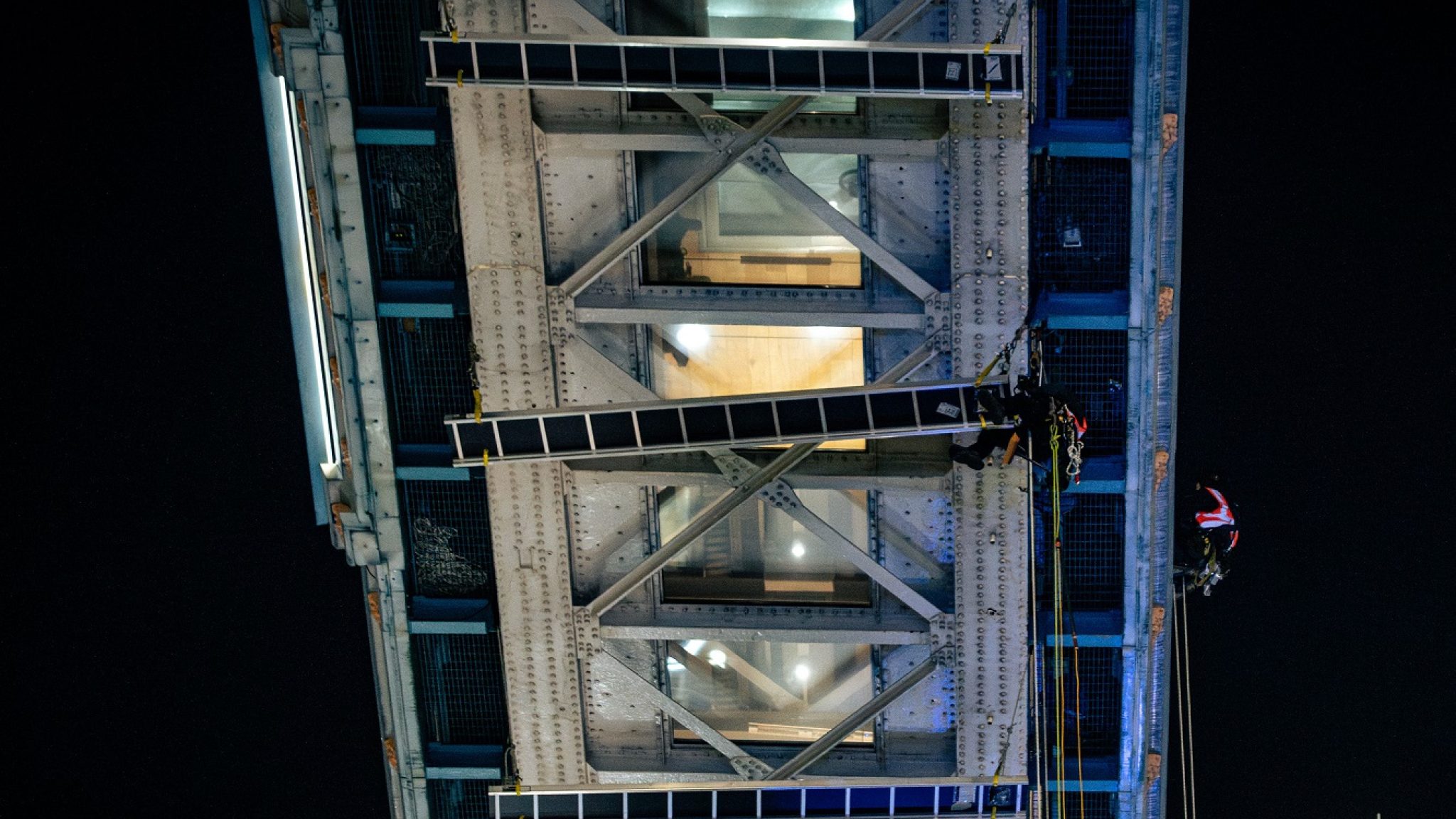 Abseiling workers suspended from the underside of the high-level walkways at Tower Bridge cleaning the glass floors
